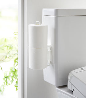 White Yamazaki Home Traceless Adhesive Toilet Paper Holder attached to the side of a toilet view 2