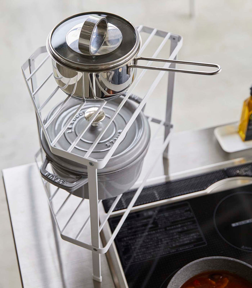 View 4 - Aerial view of White Two-Tier Corner Riser holding pot and saucepan in kitchen by Yamazaki Home.