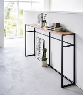 Diagonal view of the Long Console Table by Yamazaki Home in black placed by a wall with decorative items. view 11