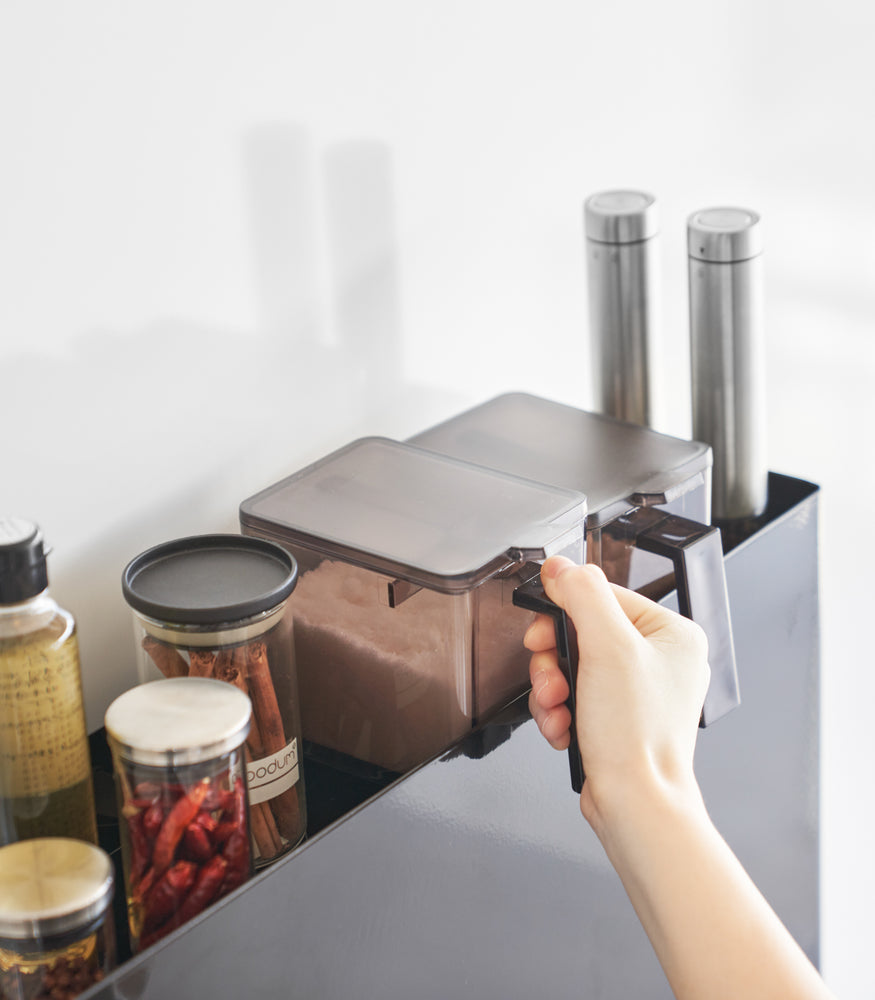 View 14 - Close up of removing spices off the top of black Yamazaki Home Two-Tier Sliding Drawer Seasoning Rack