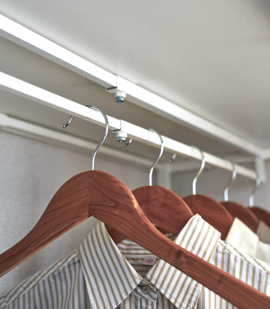 View 8 - Close up of shirts hung underneath a white Yamazaki Home Expandable Suitcase Rack