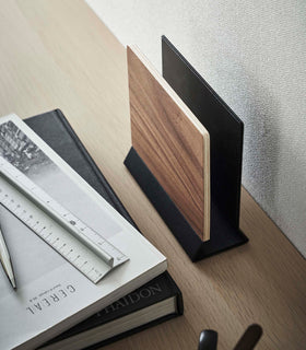 A side-view profile of a narrow wooden stand with a black metal base positioned by books on top of a desk. view 16