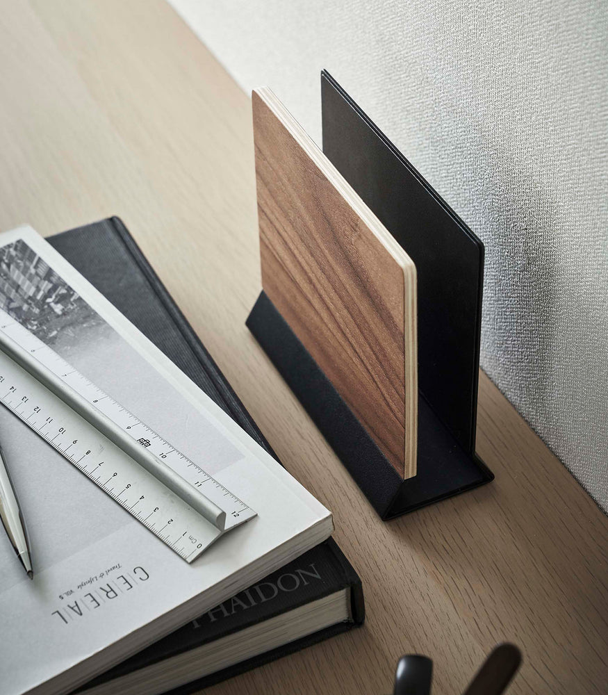 View 16 - A side-view profile of a narrow wooden stand with a black metal base positioned by books on top of a desk.