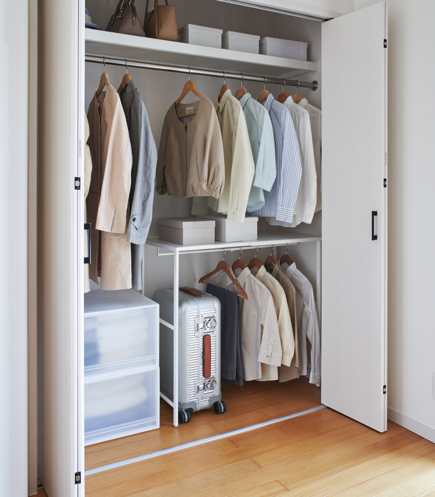 View 6 - White Yamazaki Home Expandable Suitcase Rack in a closet with a suitcase and clothes hung underneath