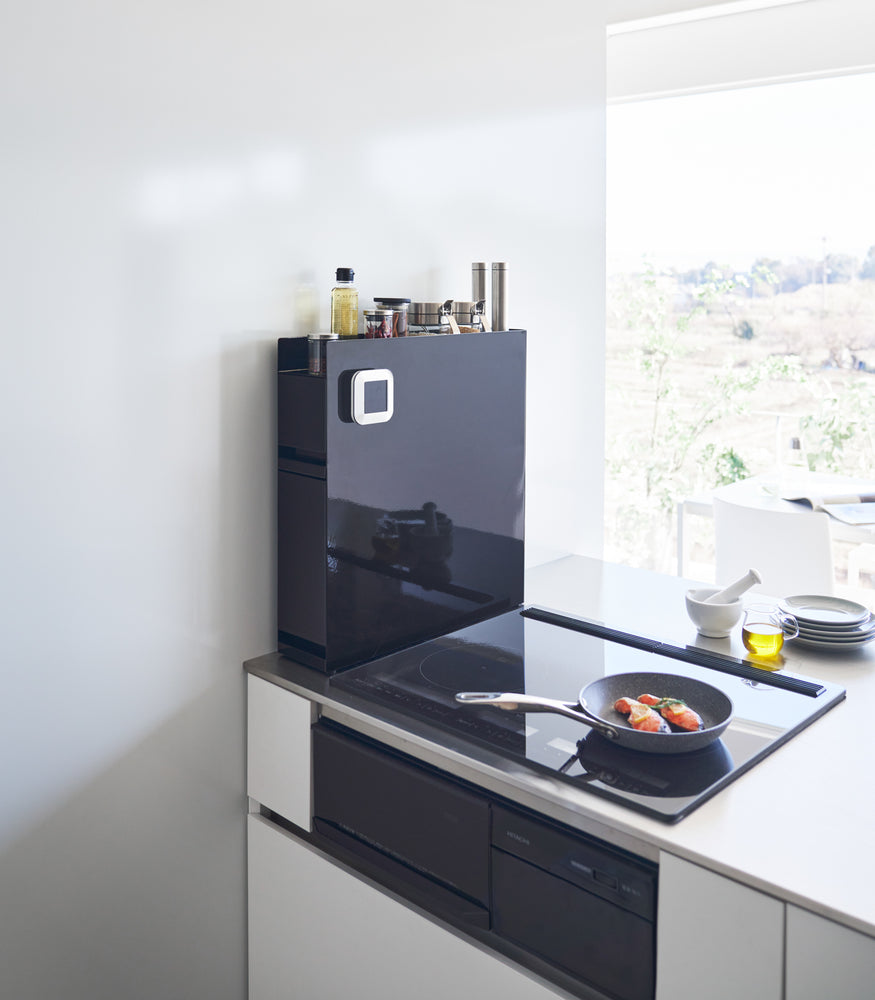 View 11 - Black Yamazaki Home Two-Tier Sliding Drawing Seasoning Rack next to a stove top