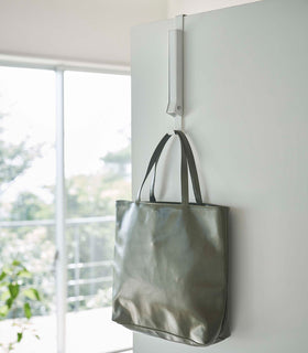 White Yamazaki Home Folding Over-The-Door Hanger closed with a purse hung view 14