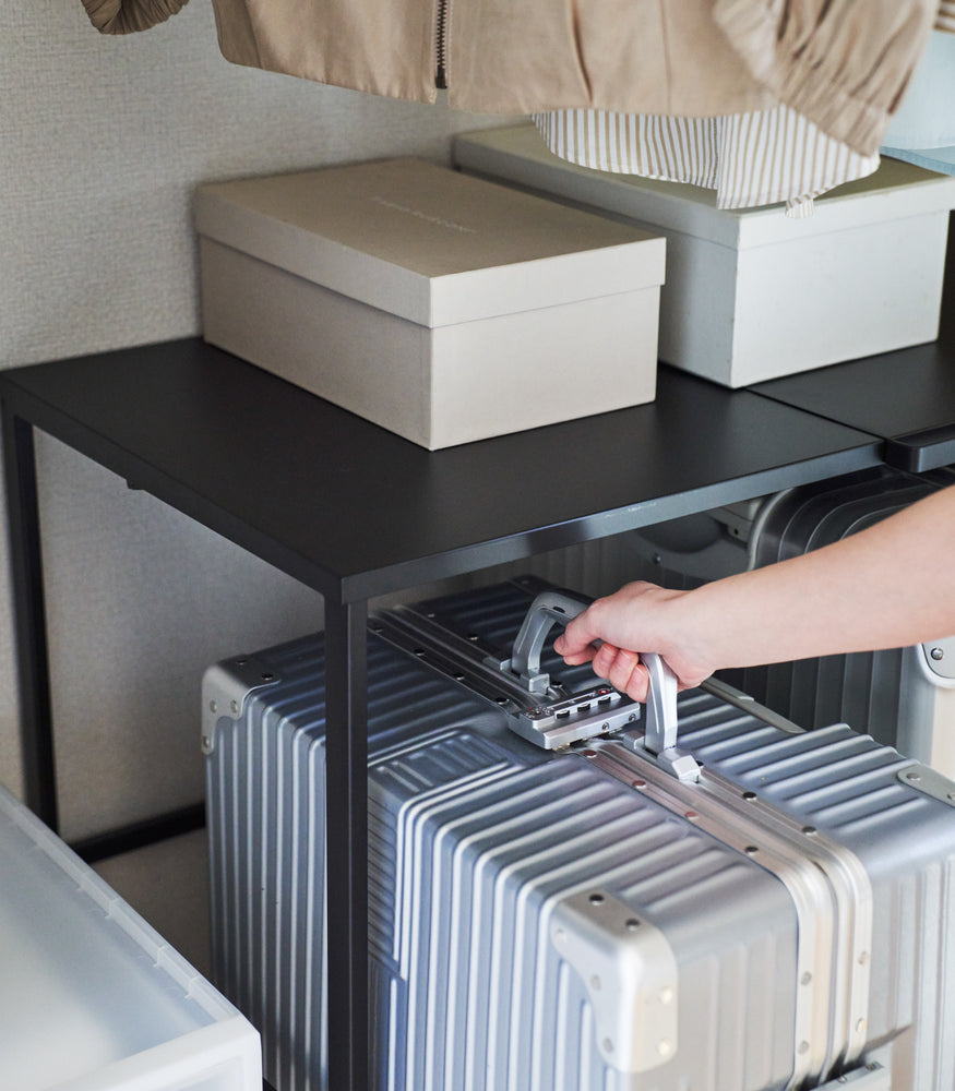 View 16 - Close up of a suitcase being removed from underneath a black Yamazaki Home Expandable Suitcase Rack