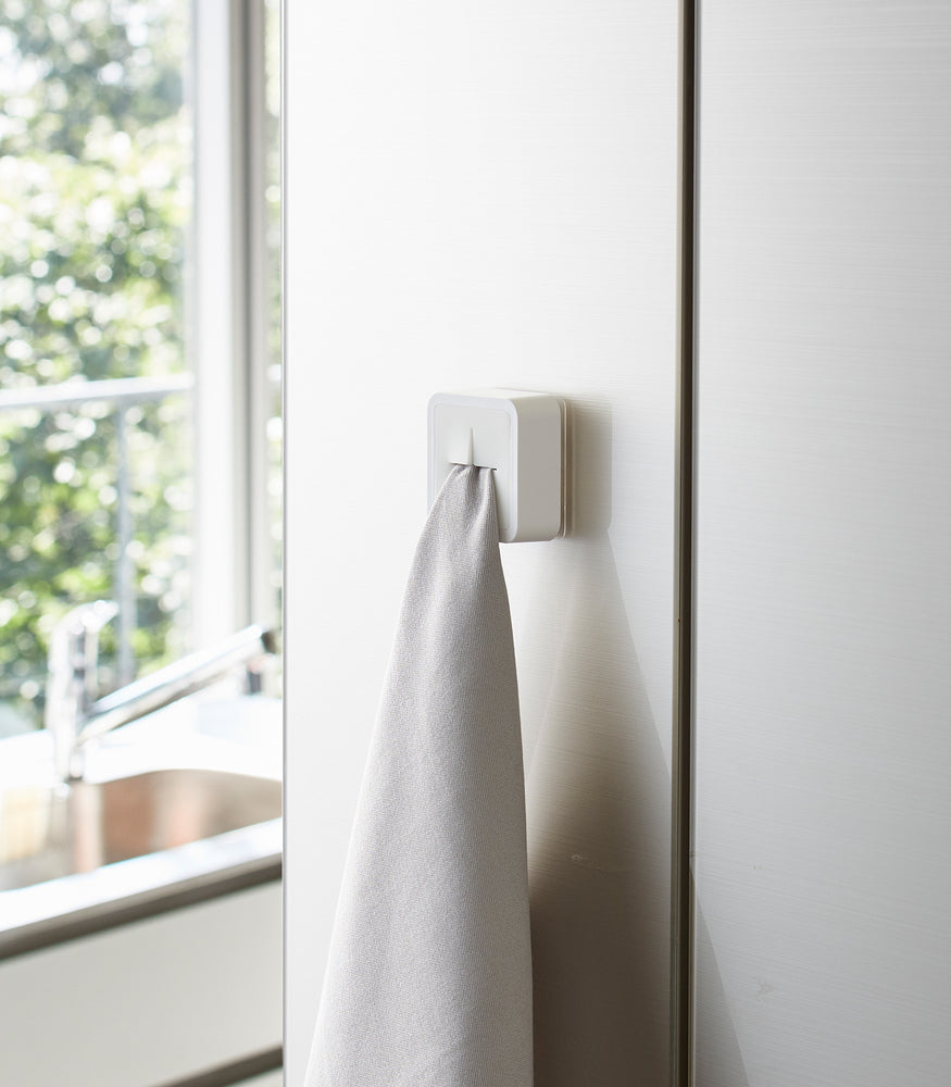 View 2 - White Yamazaki Home Traceless Adhesive Towel Holder attached to a cabinet with a towel inserted