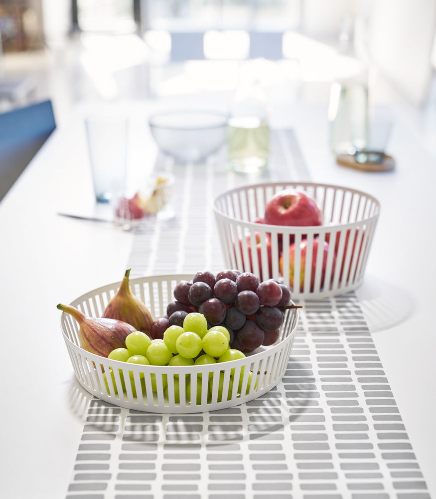 View 2 - Front view of white Fruit Basket holding fruit on dining table by Yamazaki Home.