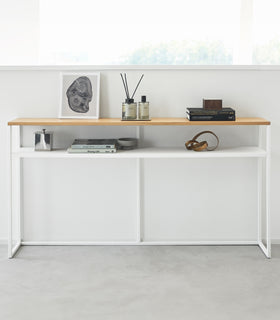 Frontal image of white Yamazaki Home Long Console Table - Shelf against a wall with books and decorations on it view 24