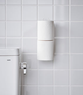 Frontal view of white Yamazaki Home Traceless Adhesive Toilet Paper Holder attached to a bathroom wall view 7