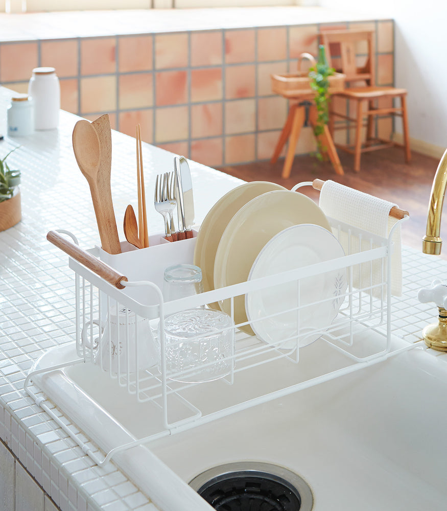 View 2 - White Over-the-Sink Expandable Dish Drying Rack holding dishware and silverware in kitchen by Yamazaki Home.