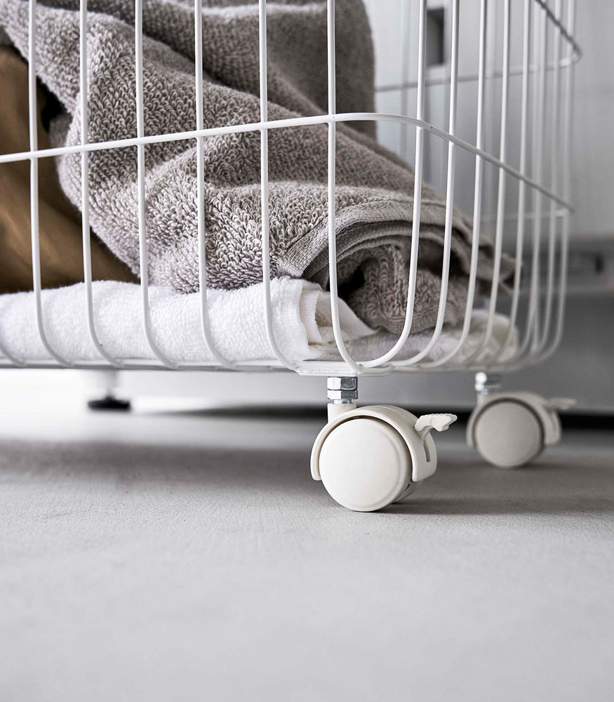 View 7 - Image showing bottom corner of Rolling Wire Basket by Yamazaki Home in white with two casters.
