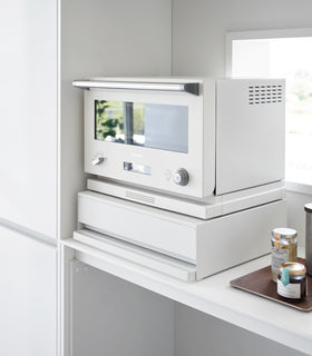 A diagonal view of the Countertop Drawer with Pull-Out Shelf by Yamazaki Home in white. Both the drawer and shelf are tucked in. A small microwave sits atop the unit. view 3