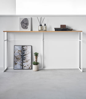 Straight view of the Long Console Table by Yamazaki Home in white placed along a wall with decorative items. view 8