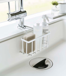 White Faucet-Hanging Sponge Caddy attached to the kitchen sink faucet and holding sponges and cleaning supplies by Yamazaki Home. view 15