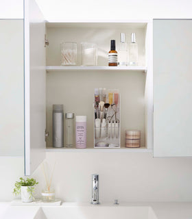 A direct view of an opened white medicine cabinet. Sunlight is focused on the right upper corner. The top half of the cabinet holds face serums and two clear containers with cotton swabs and rounds. view 23