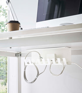 Under-Desk Cable Organizer in white by Yamazaki Home mounted under a desk holding cables. view 3