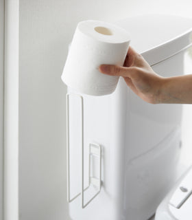 Placing a toilet paper roll on a white Yamazaki Home Traceless Adhesive Toilet Paper Holder view 4