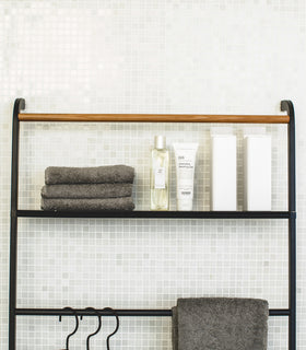 Close up front view of black Leaning Ladder Rack with Shelf holding towels and skin care products in bathroom by Yamazaki Home. view 22