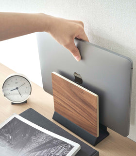 A hand lifts a closed laptop from a narrow wooden stand positioned on top of a desk. view 15