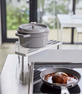 Front view of White Corner Riser holding pot next to kitchen stovetop by Yamazaki Home. view 3