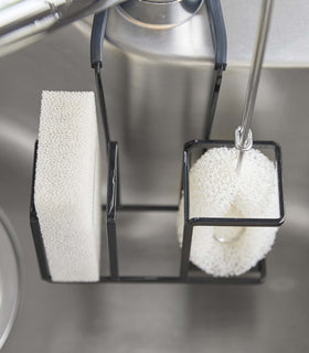 Close up top-down view of black Steel Yamazaki Home Faucet-Hanging Sponge & Brush Holder holding a sponge and a brush view 12
