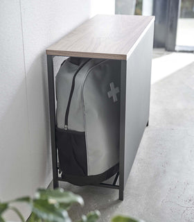 Black Yamazaki Discreet Entryway Storage Shelf against a wall with a backpack inside view 12