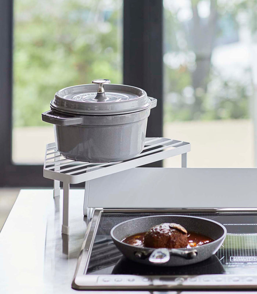 View 2 - Front view of White Corner Riser holding pot next to kitchen stovetop by Yamazaki Home.