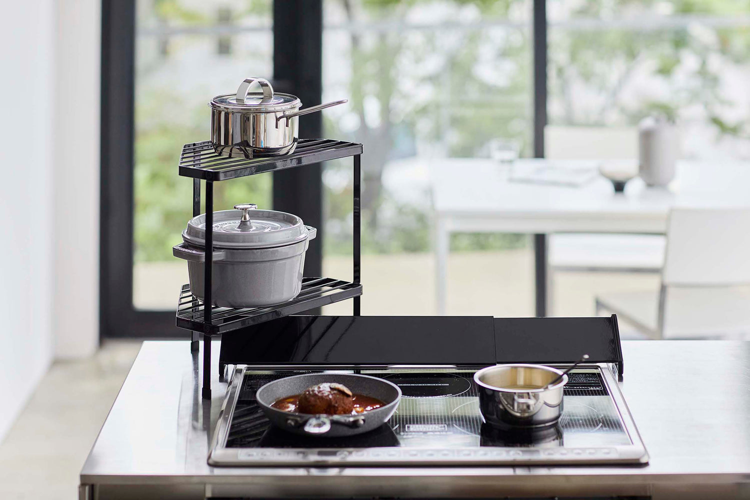 View 9 - Front view of Black Two-Tier Corner Riser holding pot and saucepan next to stovetop by Yamazaki Home.