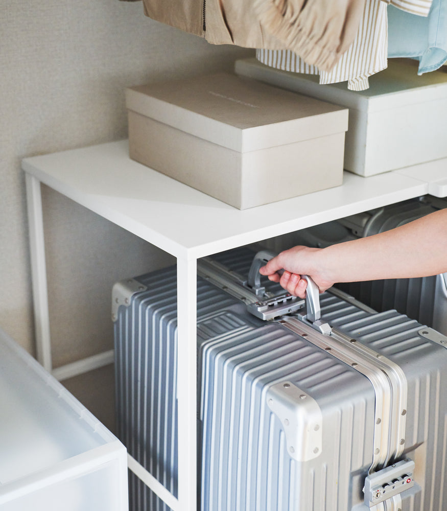 View 7 - Close up of a suitcase being removed from underneath a white Yamazaki Home Expandable Suitcase Rack