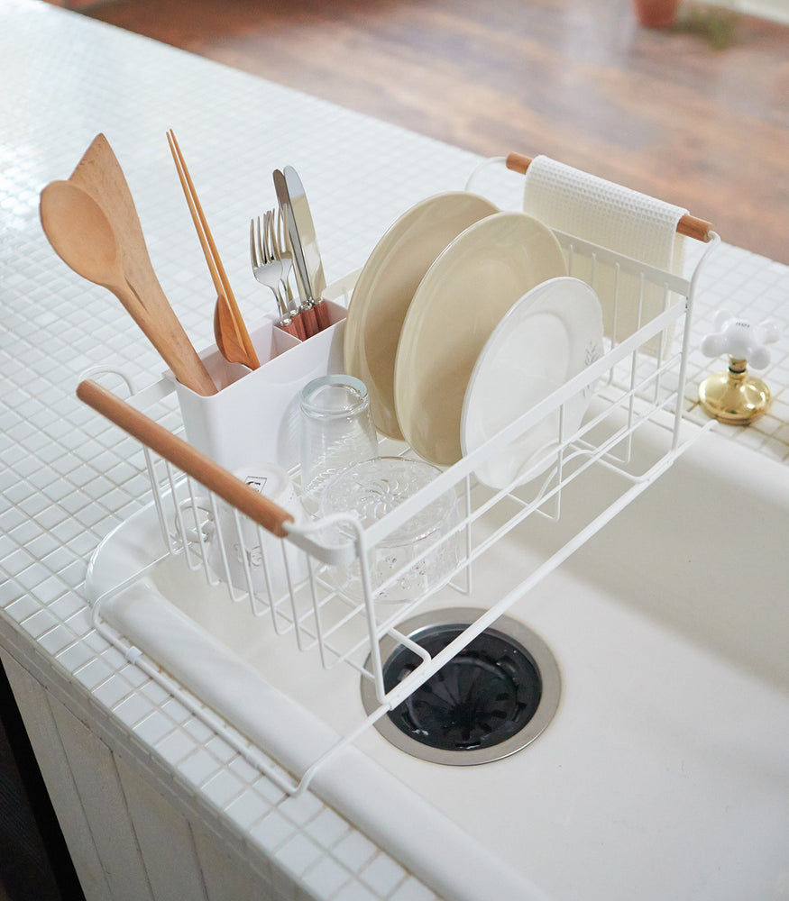 View 3 - White Over-the-Sink Expandable Dish Drying Rack holding dishware in kitchen by Yamazaki Home.