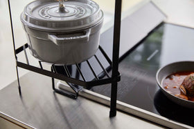 Close up bottom view of Black Two-Tier Corner Riser holding saucepans next to stovetop by Yamazaki Home. view 12