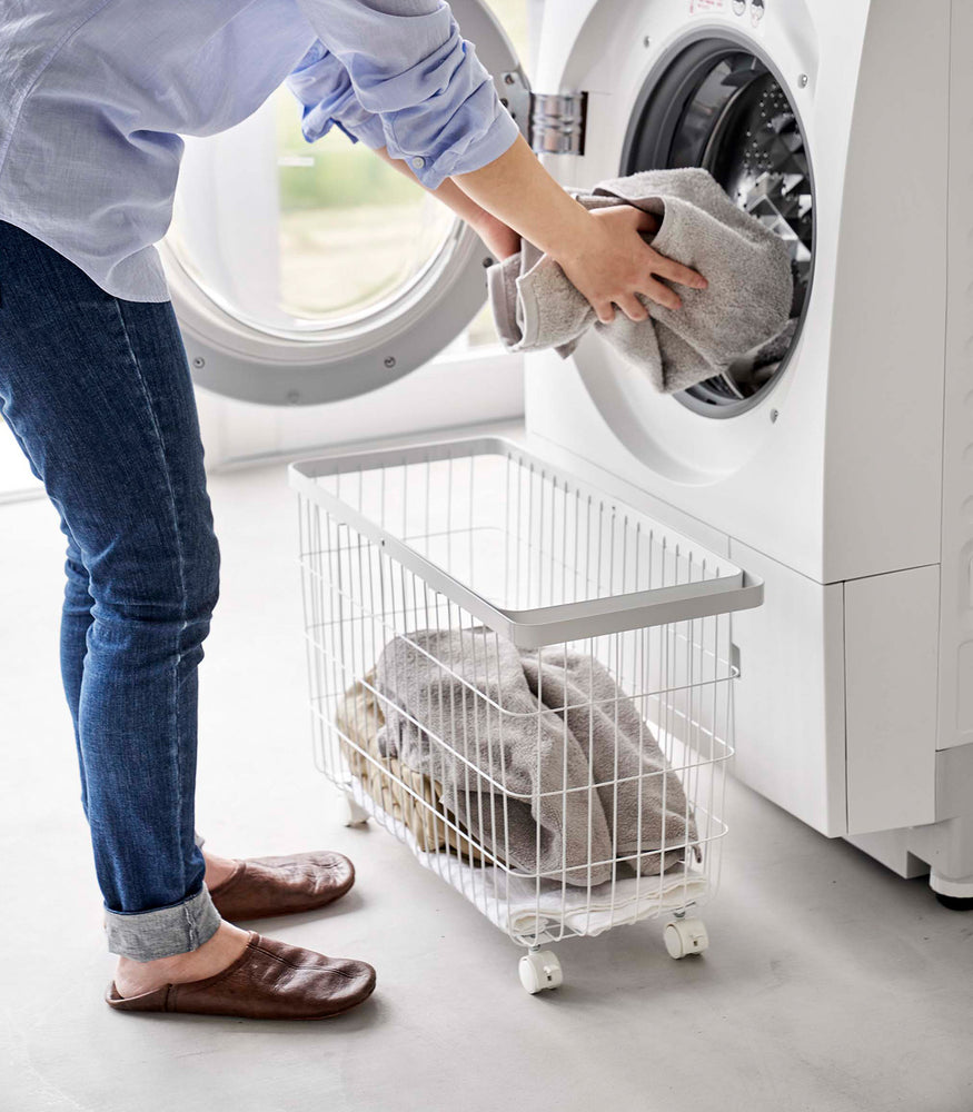View 8 - A person unloading laundry from a dryier into the Rolling Wire Basket by Yamazaki Home in white.