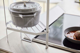 Close up bottom view of White Two-Tier Corner Riser holding saucepans next to stovetop by Yamazaki Home. view 6