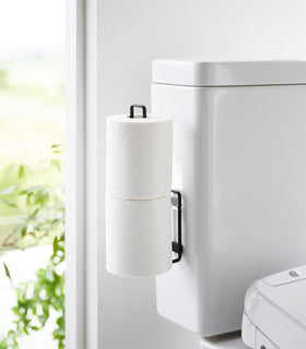 Black Yamazaki Home Traceless Adhesive Toilet Paper Holder attached to a toilet with rolls stored view 10