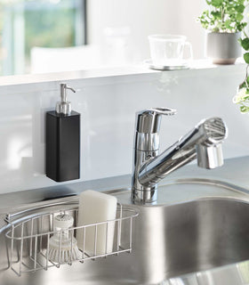 Black Yamazaki Home square soap dispenser hooked in front of kitchen sink view 9