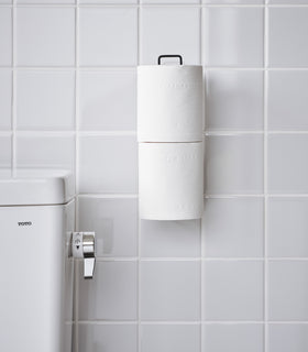 Frontal view of black Yamazaki Home Traceless Adhesive Toilet Paper Holder attached to a bathroom wall view 15