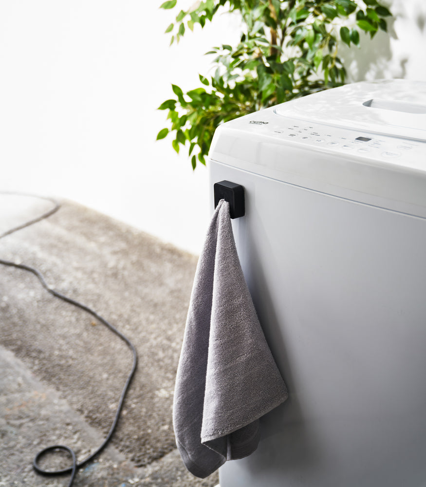 View 16 - Black Yamazaki Home Traceless Adhesive Towel Holder attached to a washing machine with a towel inserted