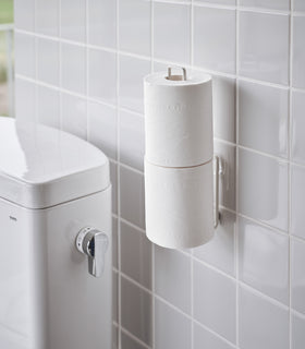 White Yamazaki Home Traceless Adhesive Toilet Paper Holder attached to a bathroom wall view 5