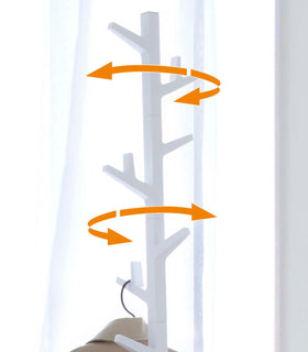 White coat rack in the shape of a tree, marked with arrows to show the movement of the rack. view 5
