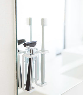 White Toothbrush Holder holding toothbrush and razor in bathroom by Yamazaki Home. view 2