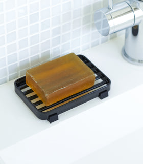 Black Slotted Soap Tray holding soap bar on sink counter by Yamazaki Home. view 6