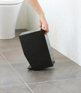 Side view of black Step Trash Can held by handle in bathroom by Yamazaki Home. view 12