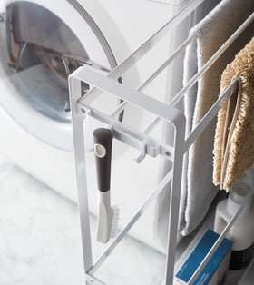 Close up corner view of white Rolling Towel Rack holding cleaning items and mats in laundry room by Yamazaki Home. view 4