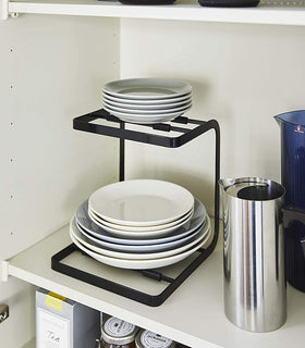Black 2-Tier Pot Holder with Hooks holding plates in kitchen cabinet by Yamazaki Home. view 11