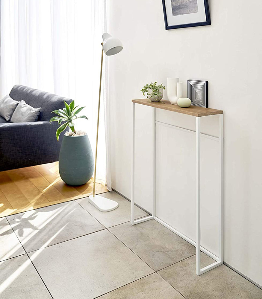 View 4 - Yamazaki Home Narrow Entryway Console Table holing a small plant next to a floor lamp. 