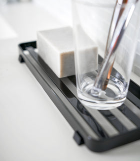 Close up side view of black Slotted Tray holding soap bar and glass in bathroom by Yamazaki Home. view 9