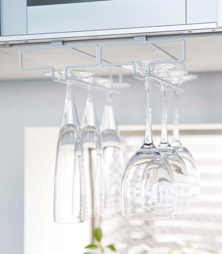 View 3 - Front view of white Undershelf Stemware Holder holding glasses by Yamazaki Home.