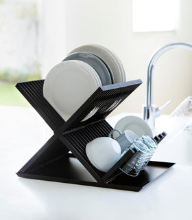 Side view of black X-Shaped Dish Rack holding plates and cups on countertop by Yamazaki Home. view 9
